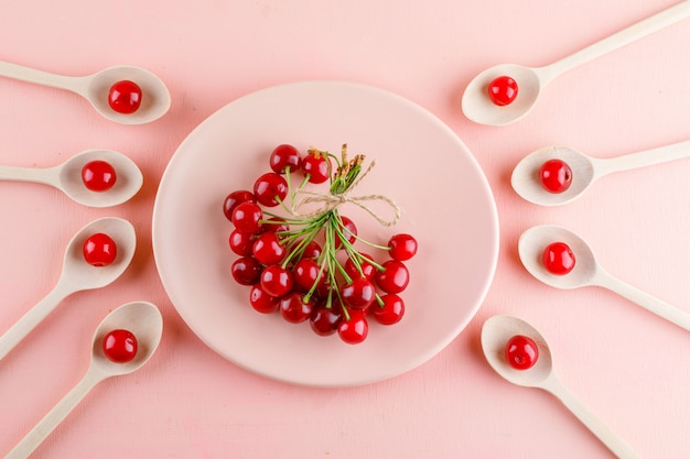 Cherries in plate and wooden spoons on a pink table. flat lay.