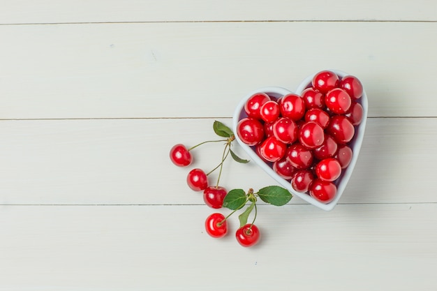 Cherries in a white bowl with leaves on wood