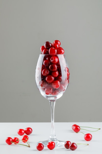 Cherries in a wine glass side view on white and grey