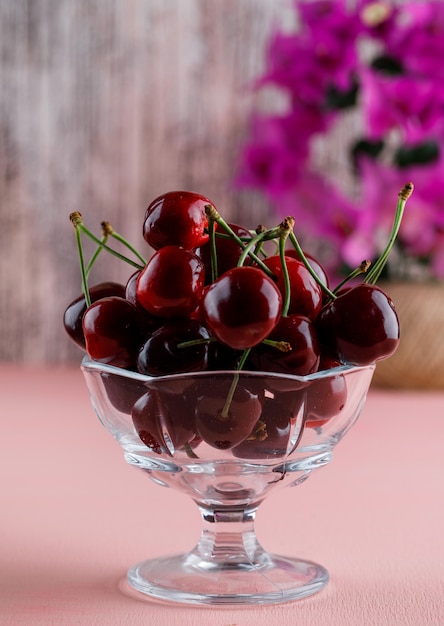 Cherries with flower pot in a vase on pink and grungy surface, close-up