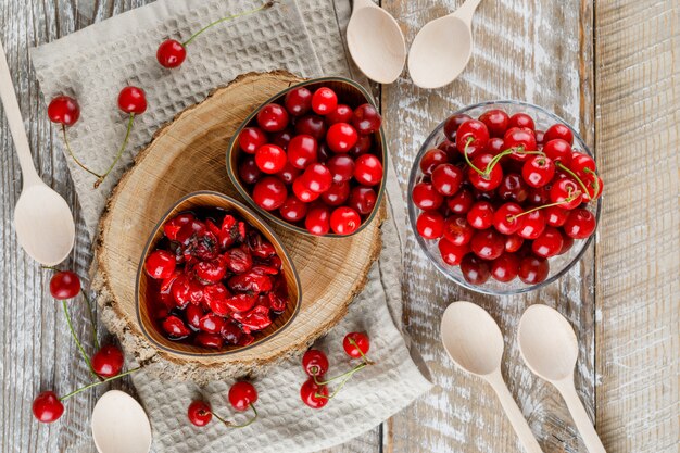 Cherries with jam, wooden board, spoons in bowls on wooden and kitchen towel