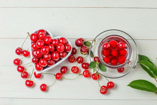 Free photo cherries with leaves in bowl and mug on wood.