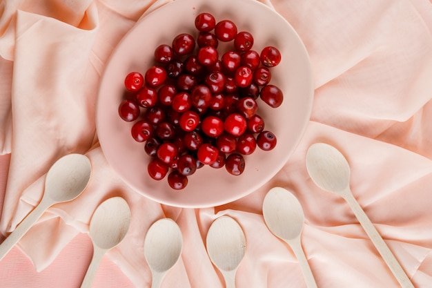 Free photo cherries with wooden spoons in a plate on textile and pink