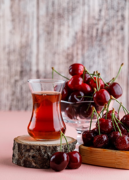 Cherries in wooden plate and vase with glass of tea on wooden board