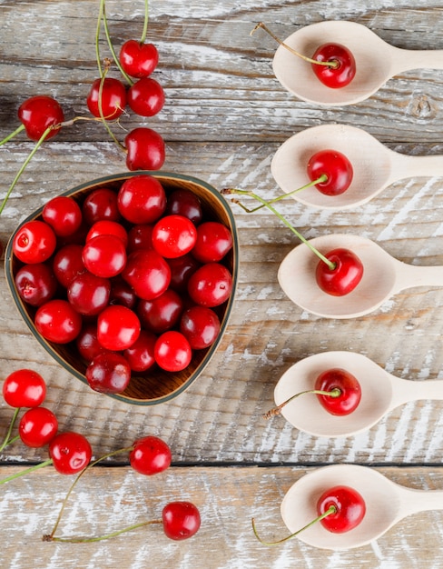 Cherries in wooden spoons and bowl on a wooden.