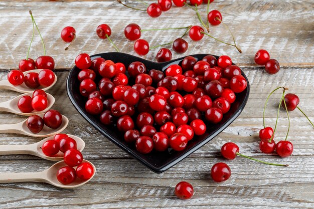 Cherries in wooden spoons and plate on a wooden.