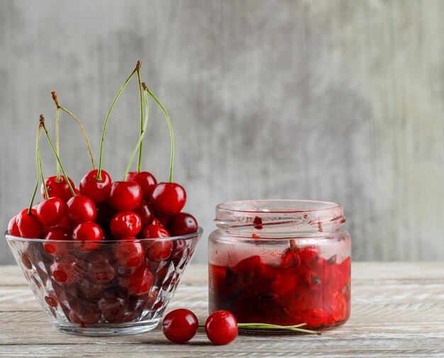 Cherry in a bowl with cherry jam side view on wooden