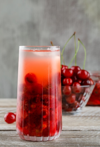 Cherry in a bowl with jam, cocktail side view on wooden