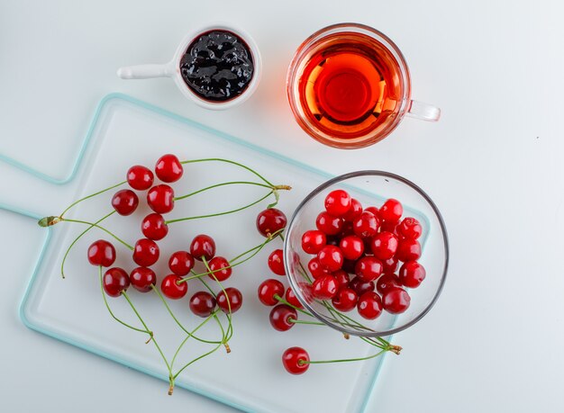 Cherry in a bowl with tea, jam flat lay on white and cutting board
