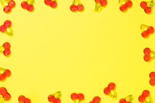 Cherry candies frame on yellow background with copy space