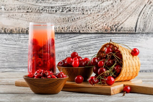 Cherry drink in a jug with cherries, jam side view on wooden and cutting board