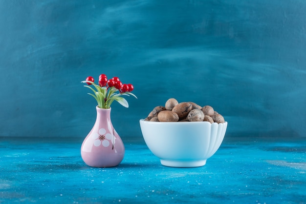 Cherry fruits in a vase next to pecan nuts in a bowl , on the blue table. 