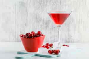 Free photo cherry juice in a glass with cherries, cutting board side view on white and grungy