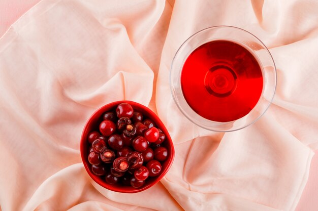 Cherry juice in a glass with cherries on pink and textile