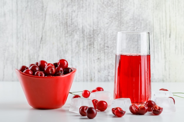 Cherry juice with cherries, ice cubes in a glass on white