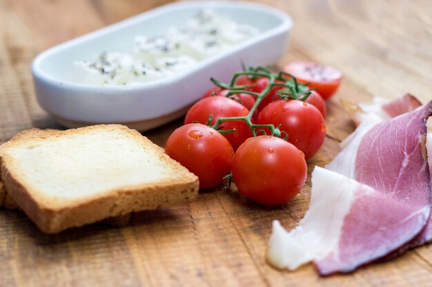 Cherry tomato, cheese and prosciutto with toast on wooden table