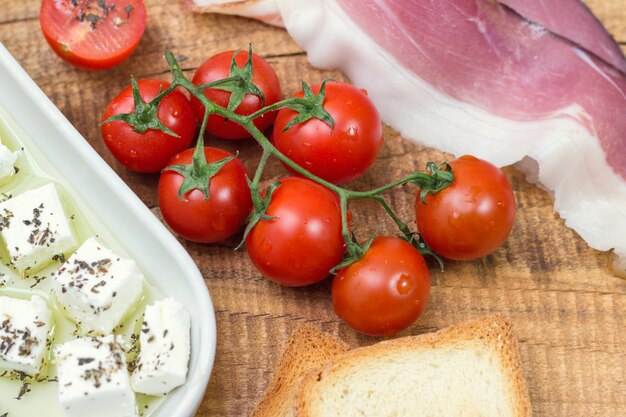 Cherry tomato, cheese and prosciutto with toast on wooden table