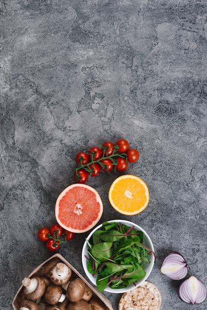 Cherry tomatoes; halved citrus fruit; spinach; mushrooms; onion and rice puffed cake on concrete backdrop