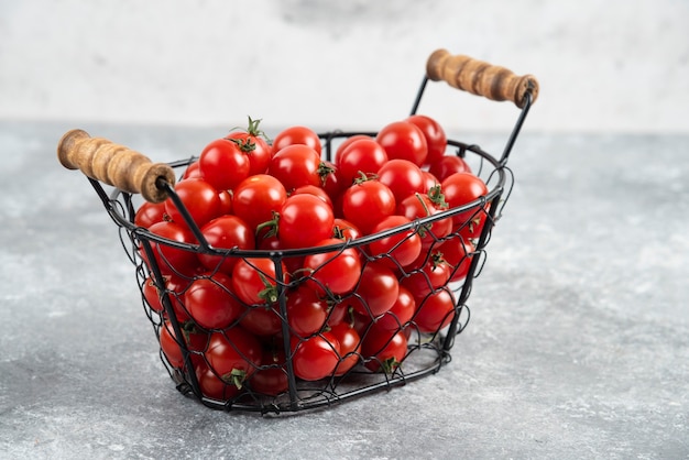 Cherry tomatoes in a metallic basket on marble table.