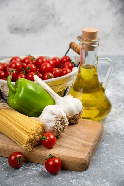 Cherry tomatoes, pastas, garlic, green pepper and olive oil on a wooden board.