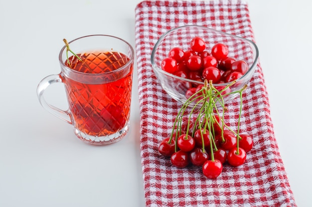 Cherry with tea in a bowl on white and kitchen towel, high angle view.