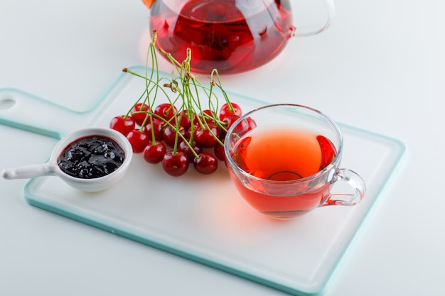 Free photo cherry with tea, jam on white and cutting board, high angle view.