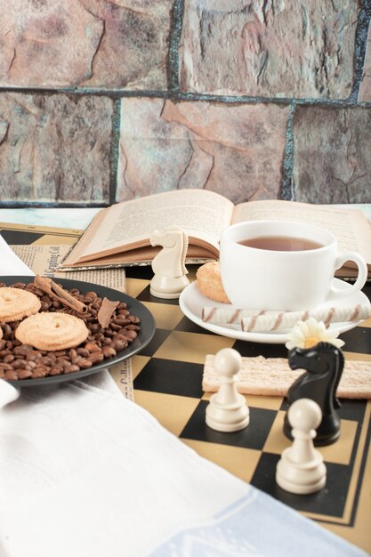 Шахматные фигуры, чашка чая, книга и печенье