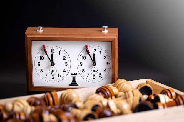 Chess pieces on a board and a chess clock on a dark background