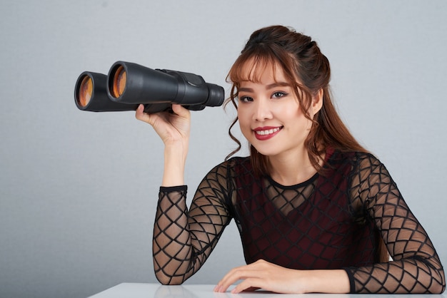 Chest up shot of cheerful woman holding the binoculars looking at camera