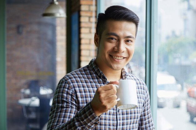 Chest-up shot of young Asian guy drinking tea in a cafe