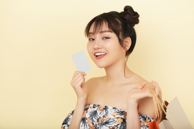 Chest up shot of young woman holding a bank card with shopping bags in her another hand