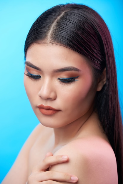 Free photo chest-up side shot of beautiful woman with dark hair and heavy makeup posing with bare shoulder