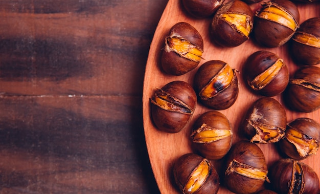 Chestnuts in a wooden plate on a dark wooden table