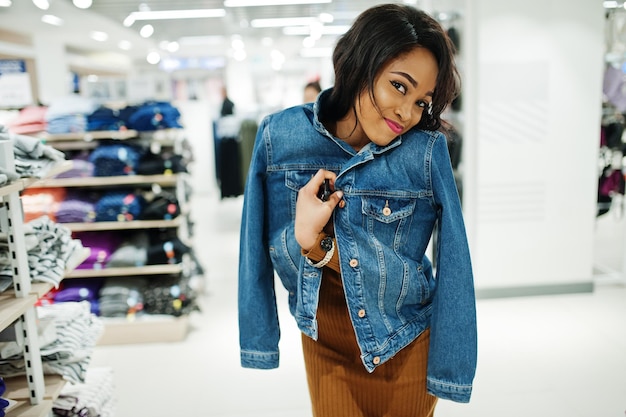 Free photo chic african american woman in brown tunic dress and jeans jacket posed at clothes store it's time for shopping