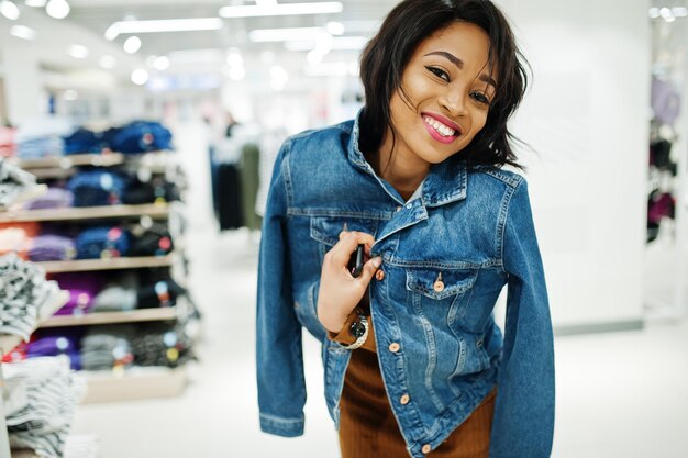 Chic african american woman in brown tunic dress and jeans jacket posed at clothes store It's time for shopping