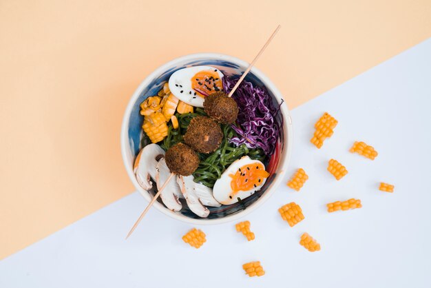 Куриные шарики в палочке над миской с салатом и яйцами на двойном фоне
