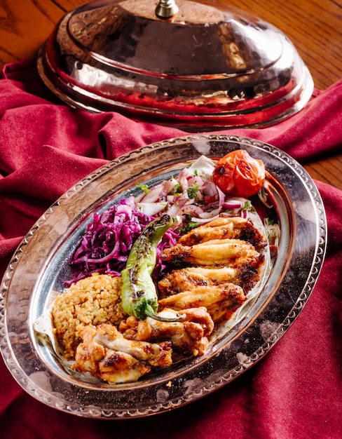 Chicken barbecue with rice garnish and vegetable salad inside ethnic plate.