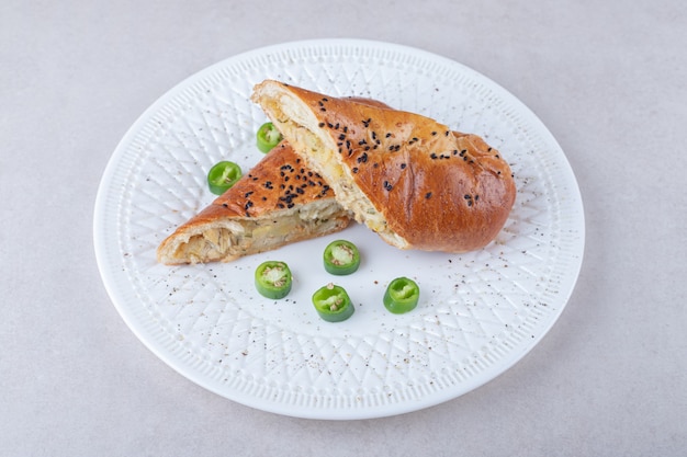 Chicken in bread next to sliced chili pepper on plate on marble table.