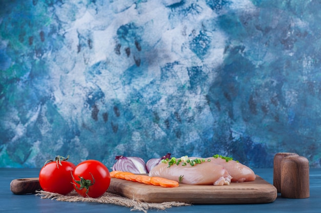 Chicken breast sliced carrots on a cutting board next to sliced onion on the blue surface