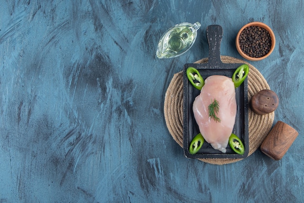 Free photo chicken breast and sliced pepper on a board on a trivet next to spice and oil bowls, on the blue background.