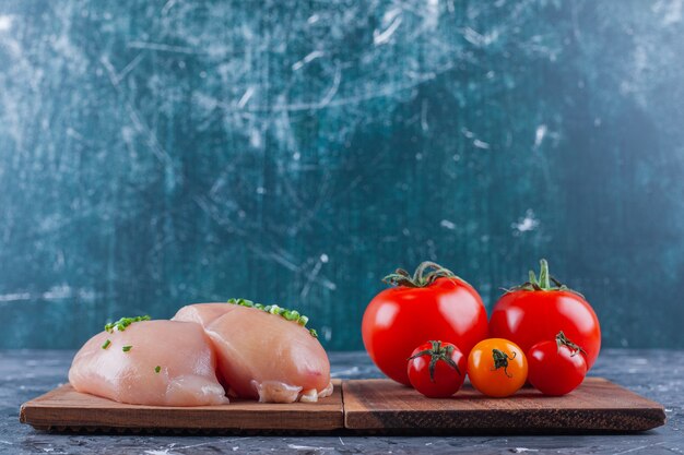 Chicken breast and tomatoes on a board on the blue surface