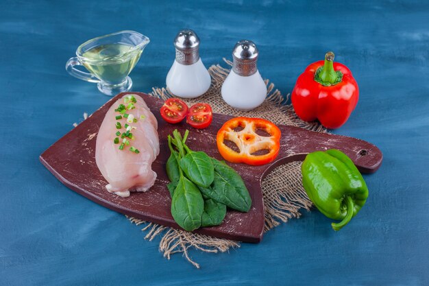 Chicken breast and vegetables on a cutting board non a burlap napkin, on the blue table.