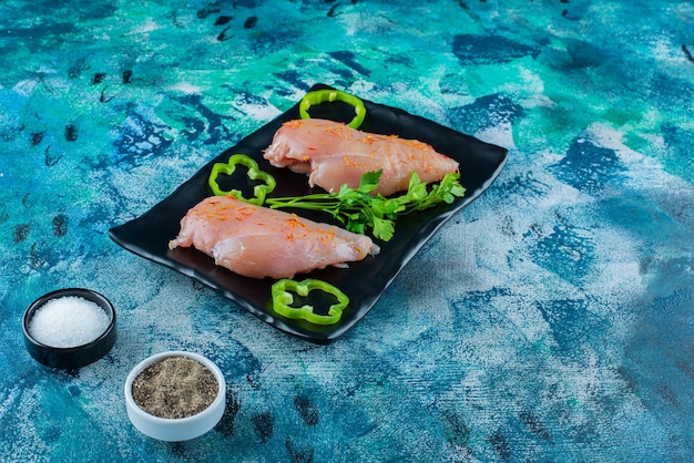 Free photo chicken breast and vegetables on a platter next to spice bowls , on the blue background.