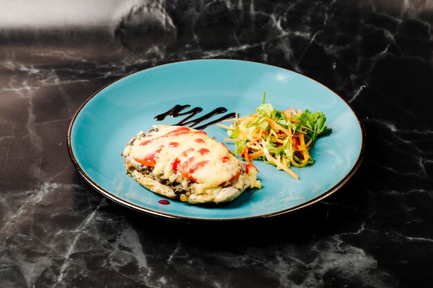 Chicken breast with melted creamy dressing and red sauce on the top and vegetable salad in green plate.