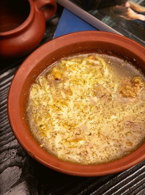 Chicken broth noodle, spaghetti soup with walnuts in pottery bowl. 