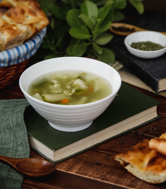 Chicken broth soup with vegetables inside a white bowl served with bread