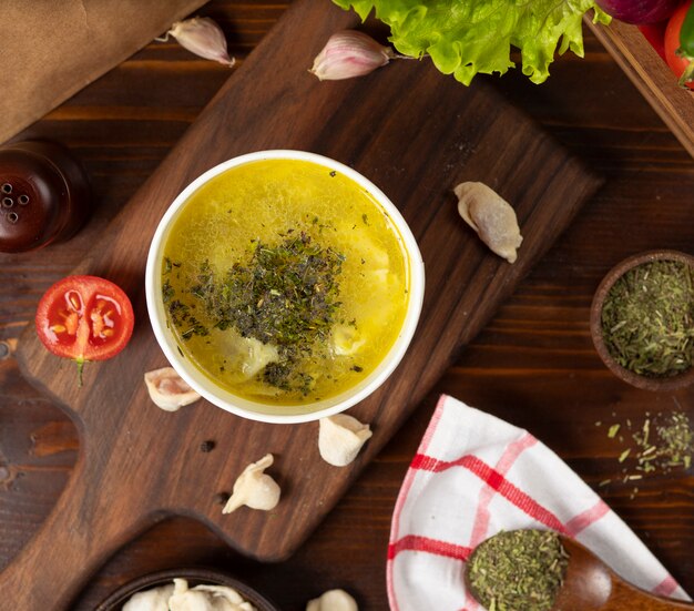 Chicken broth with herbs soup in disposable cup bowl served with green vegetables.