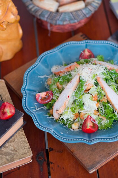 Chicken caesar salad with chopped parmesan cheese fresh lettuce and tomatoes, crackers in blue plate.