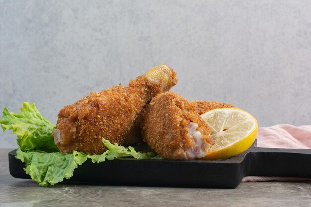 Chicken crispy legs with lettuce and lemon on dark board.