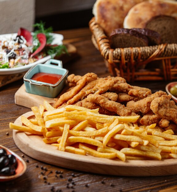 chicken croquettes served with french fries on wooden platter and fresh salad